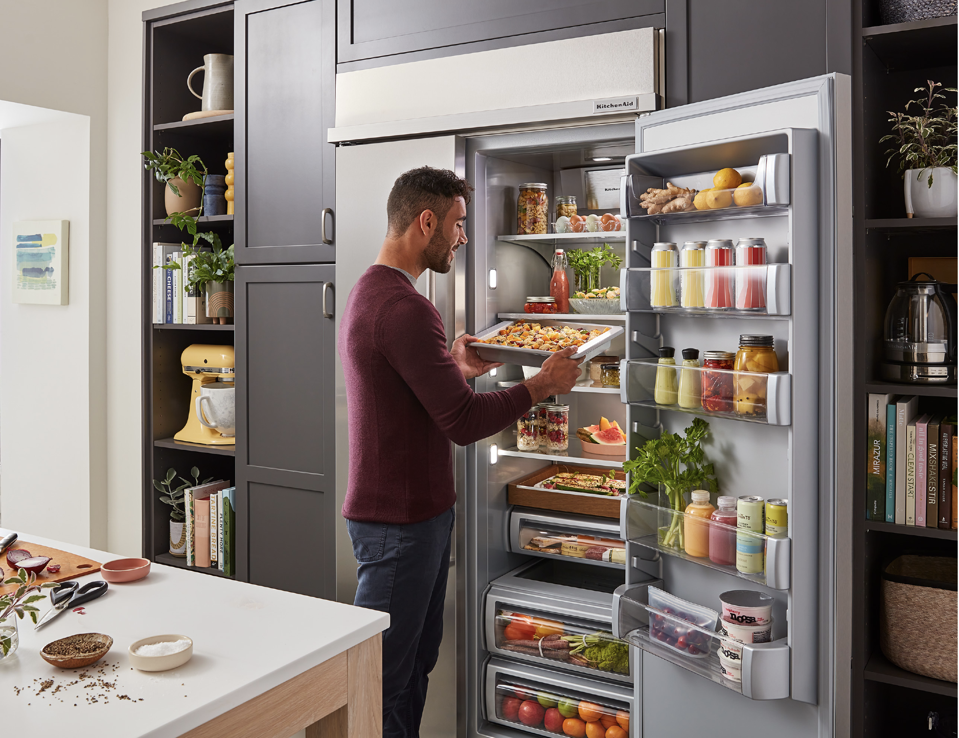 a man getting food out of a full, built-in KitchenAid refrigerator